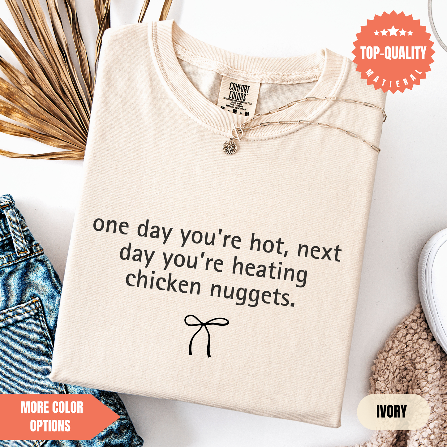 a beige t-shirt with a humorous text printed on it, along with a small bow and some other items such as jeans and a sweater.
