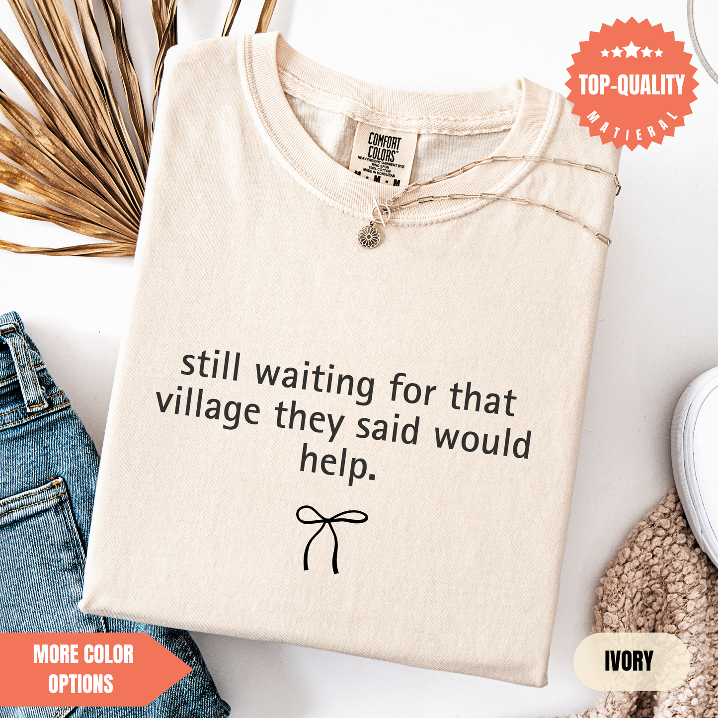 a beige t-shirt with a humorous text printed on it, along with a small bow design. The t-shirt is displayed on a white background, and there are some other items, such as jeans and a sweater, visible in the background.