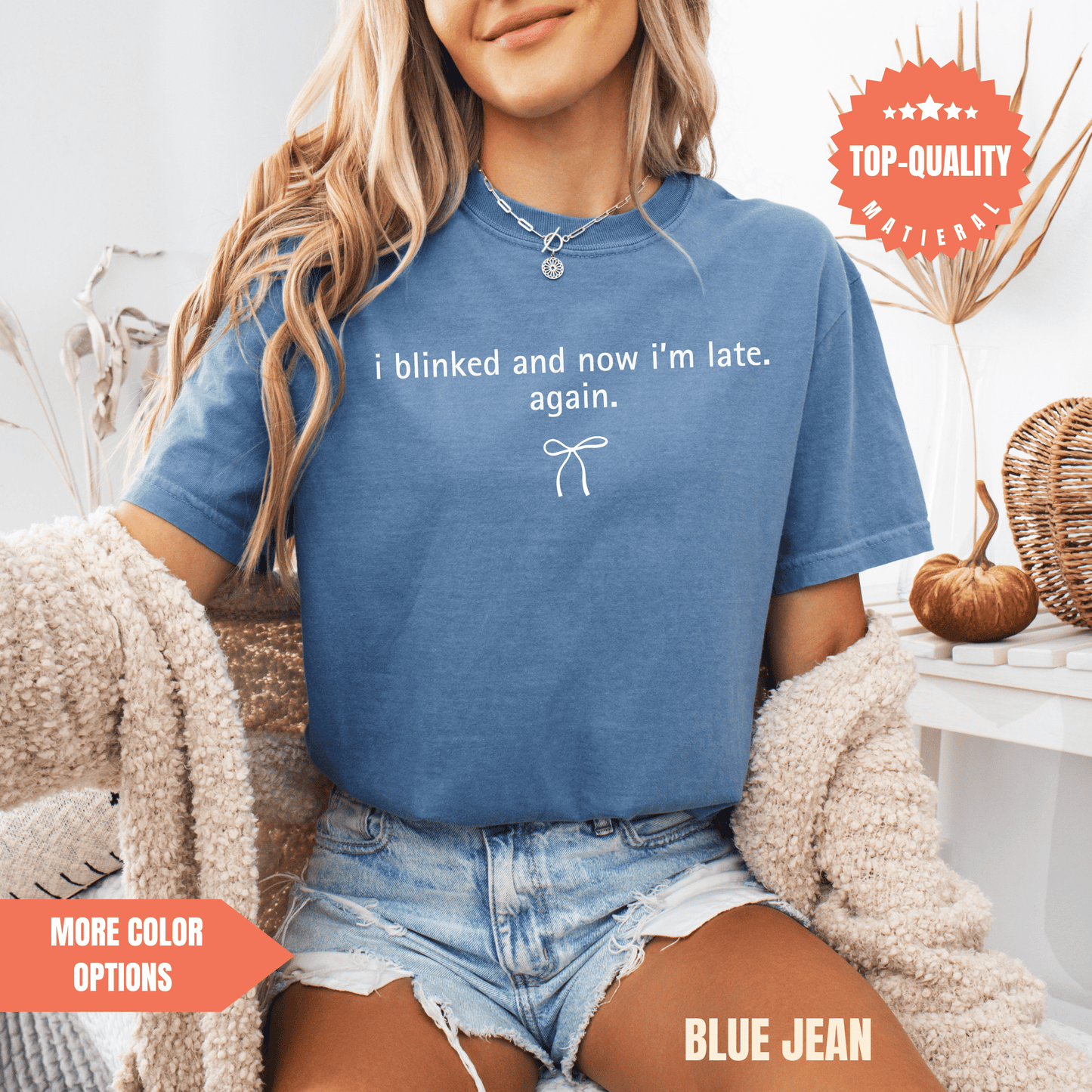 A woman wearing a blue t-shirt with a humorous text and denim shorts is sitting in a chair.