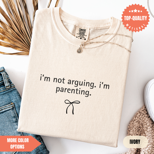 a beige t-shirt with a humorous text printed on it, along with a small bow and some other clothing items.