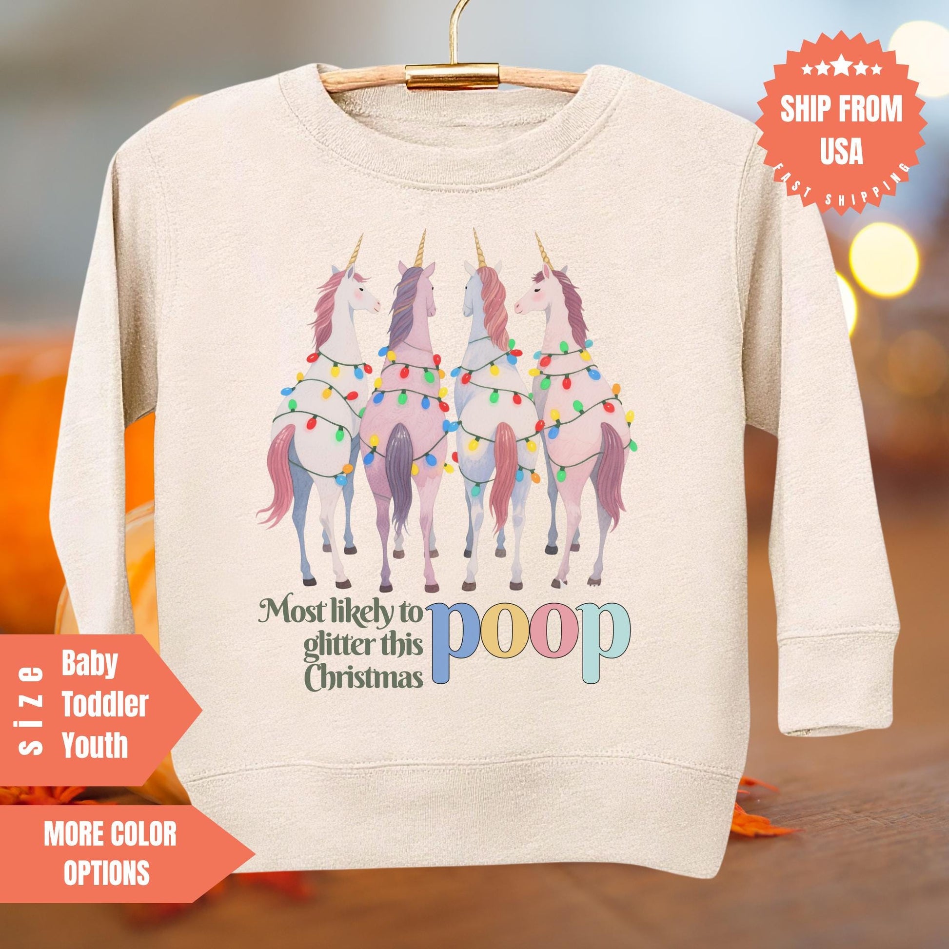 A beige sweater with a graphic design of four unicorn horses with glittery Christmas lights around their necks. The text on the sweater says "Most likely to glitter this Christmas".