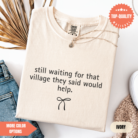 a beige t-shirt with a humorous text printed on it, along with a small bow design. The t-shirt is displayed on a white background, and there are some other items, such as jeans and a sweater, visible in the background.