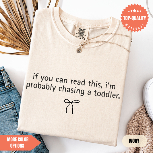 a beige t-shirt with a humorous text printed on it, along with a small bow and some other clothing items.